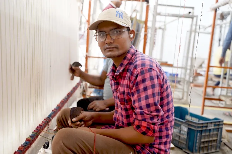Arjun Yadav guiding a younger apprentice weaver at the loom